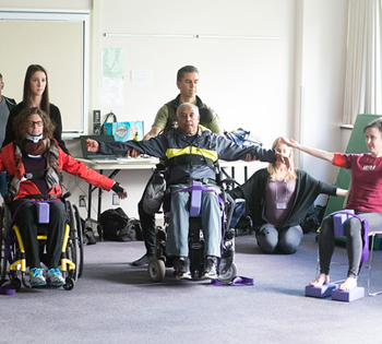 people in wheelchairs do arm stretches in yoga class